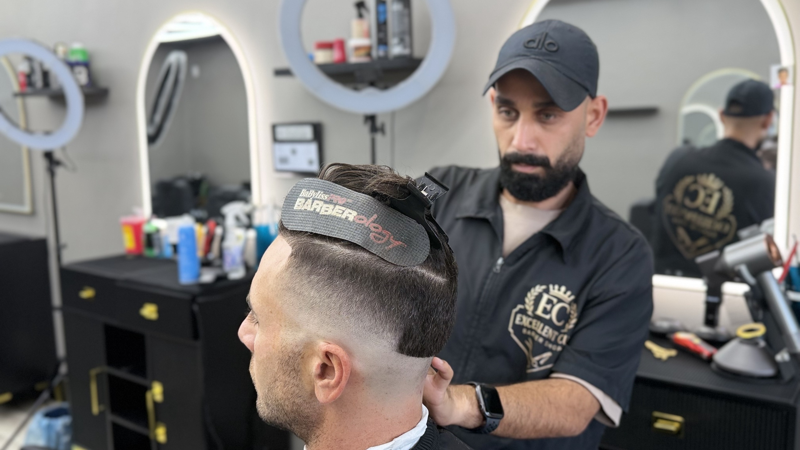 Experience an elite grooming environment designed for comfort and style in Mission Valley. Luxury barbershop interior with dark walls, large mirrors, and warm ambient lighting