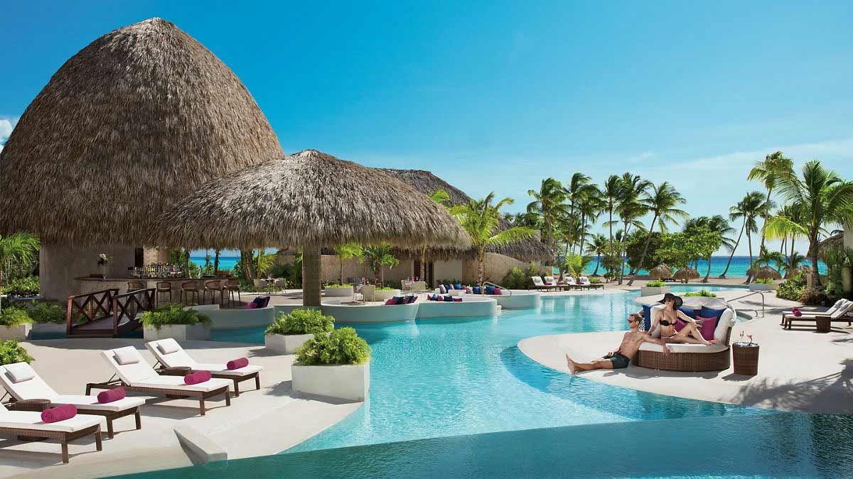 The exclusive atmosphere of Cap Cana offers a level of privacy that couples over 30 appreciate. Luxury outdoor lounge area at a tropical resort with white curtains and palm trees in the background.
