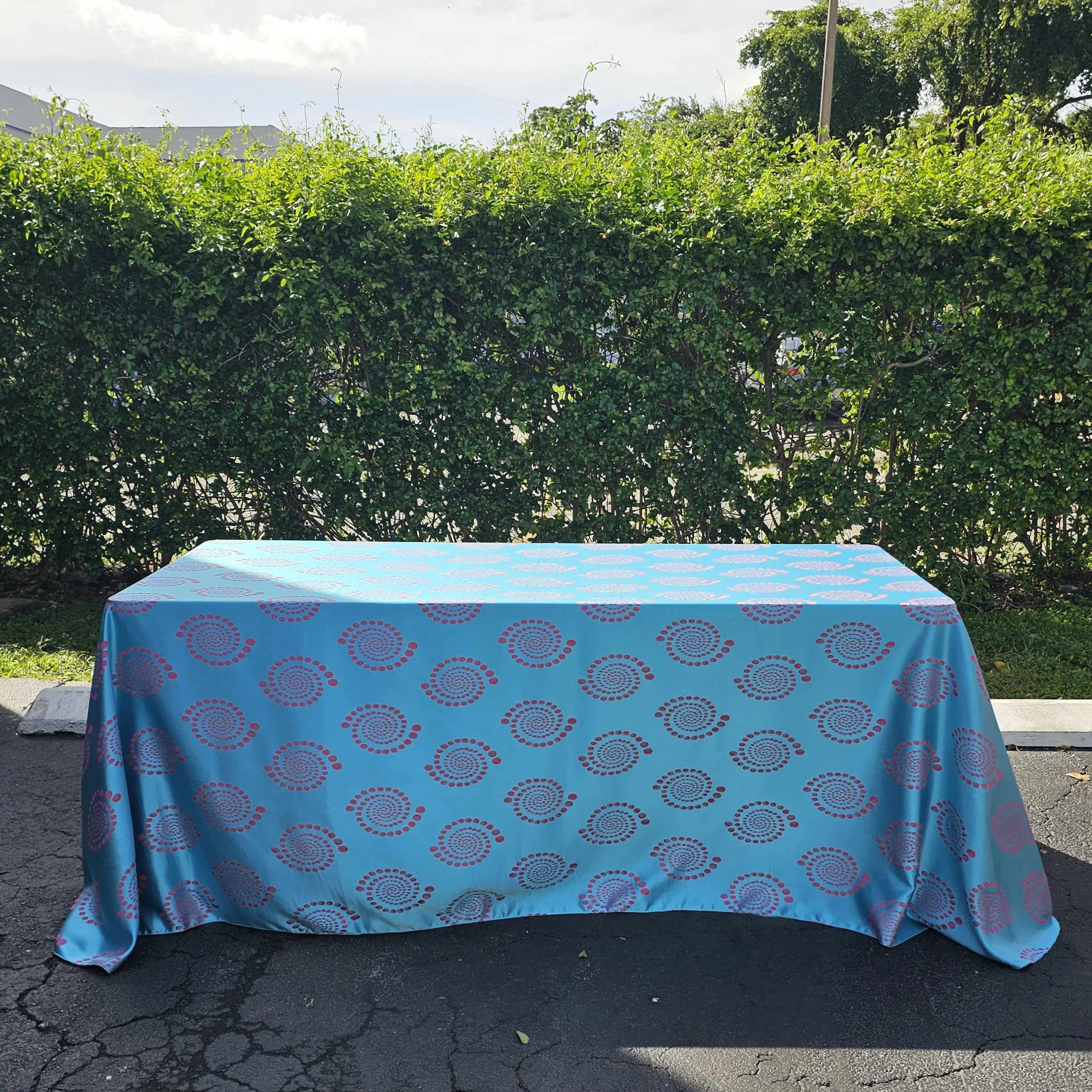 A perfect floor-length drop requires precise measurements that stock sizes often miss. A professional smoothing a floor-length ivory tablecloth over a round table in a banquet hall.