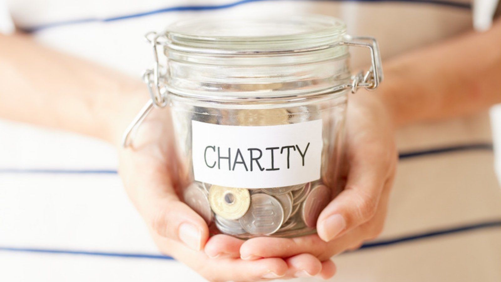 Hands holding a glass charity collection jar full of coins, showing why to check a charity appeal is genuine before donating