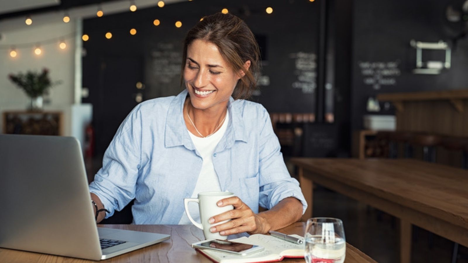 Woman using a laptop in a coffee shop on public Wi-Fi, What a VPN Actually Protects You From, and What It Doesn't