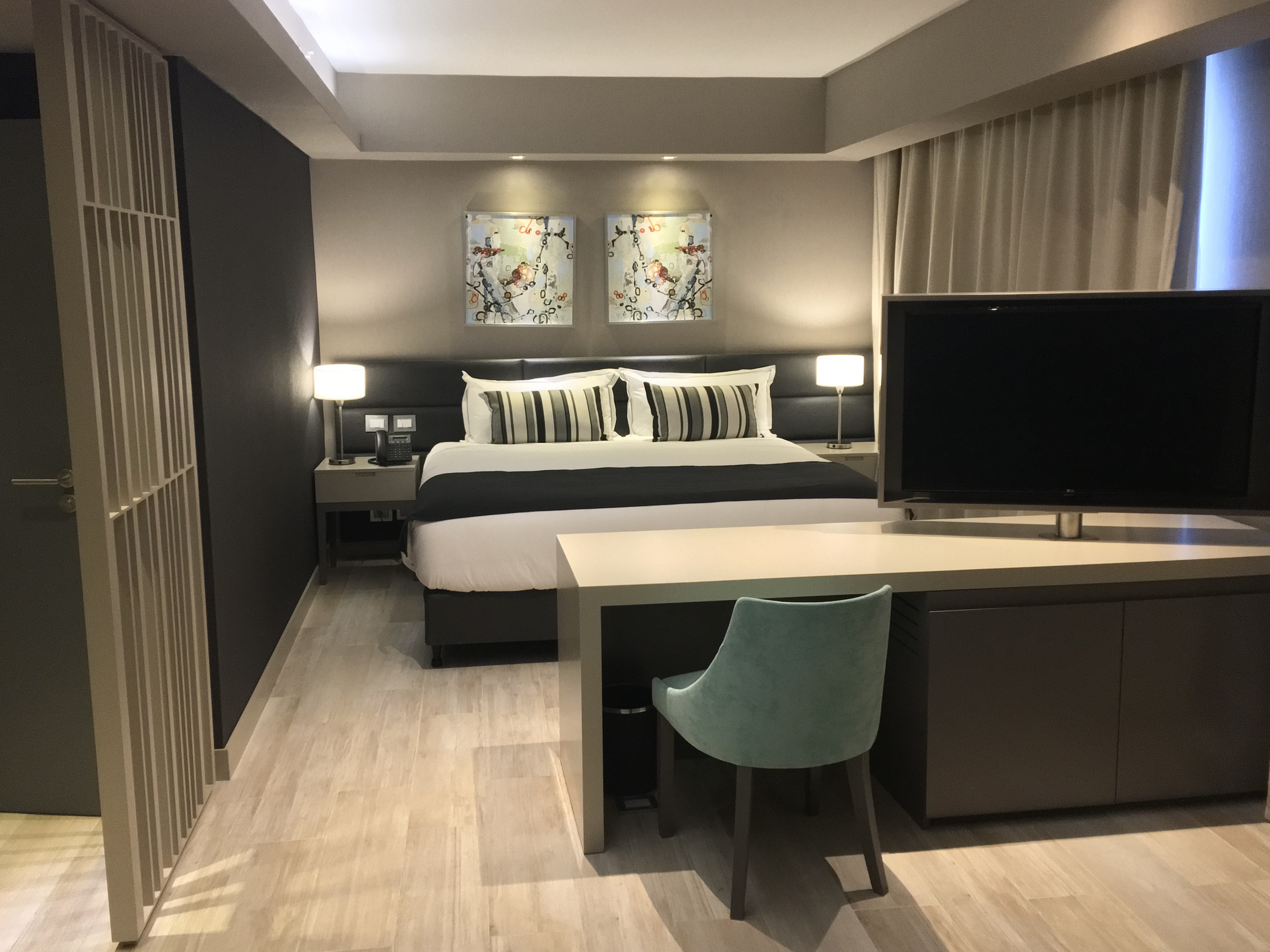 Habitación de hotel moderna con cama grande, arte abstracto, escritorio con silla azul y televisor.