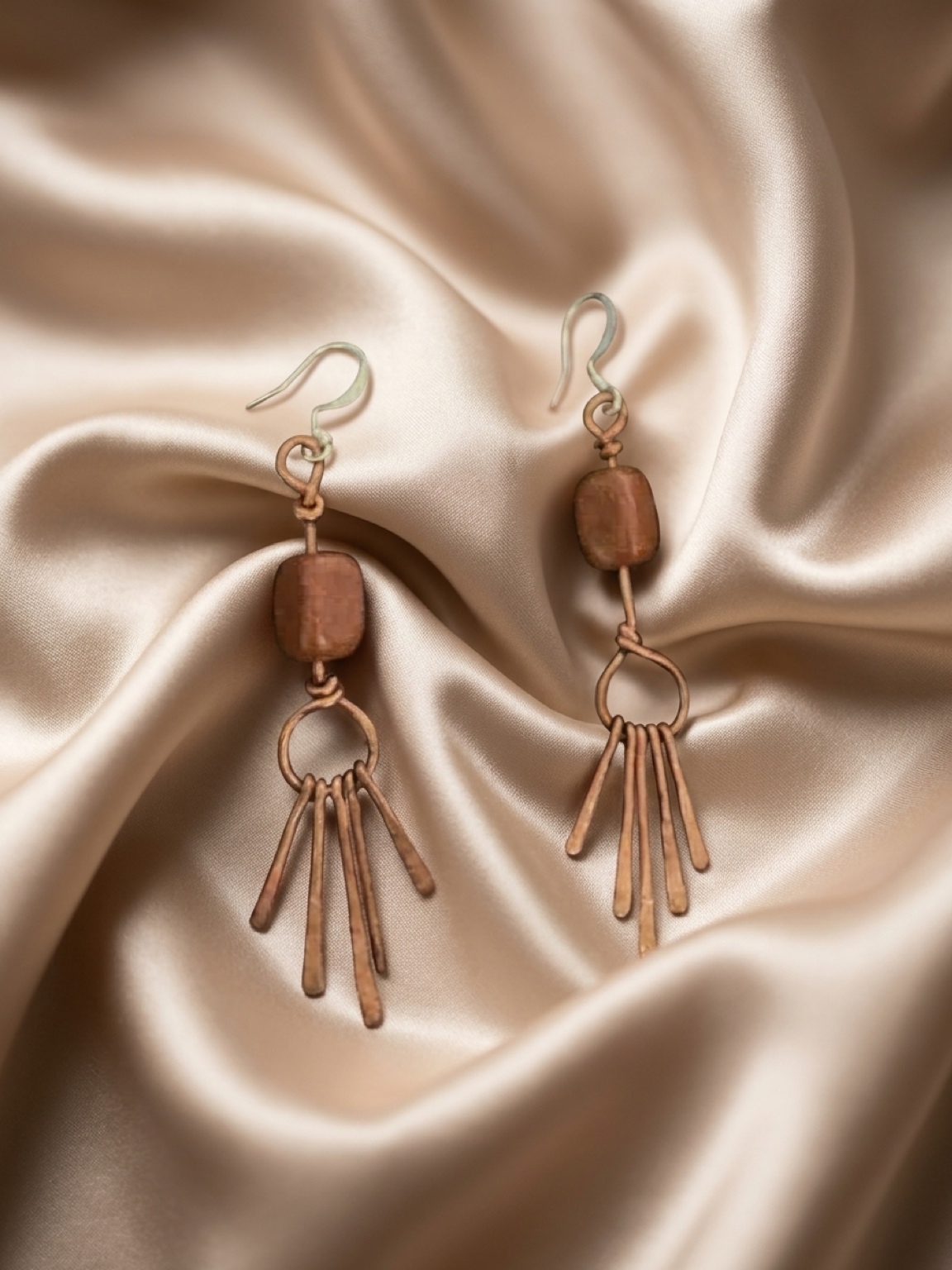Simplicity meets artistry: wire-wrapped drops are perfect for an effortless morning look. A pair of copper wire-wrapped earrings with small gemstones laid flat on a neutral linen fabric in natural light.